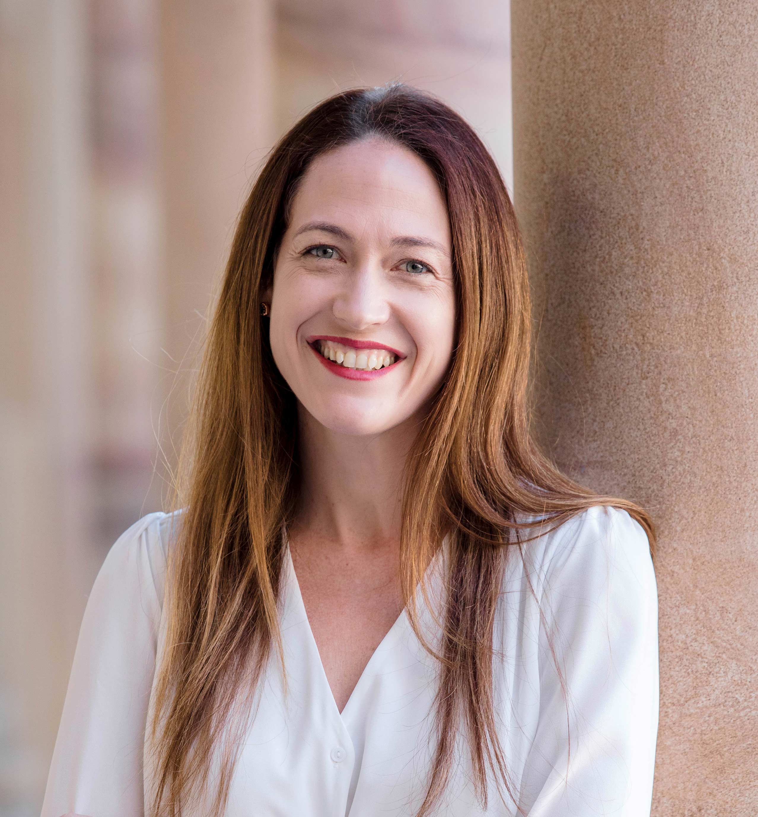 Pro-Vice-Chancellor (Global Engagement and Entrepreneurship) Dr Jessica Gallagher leaning against a sandstone column in the Great Court