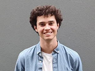 Thomas smiling and wearing white shirt under denim button down.