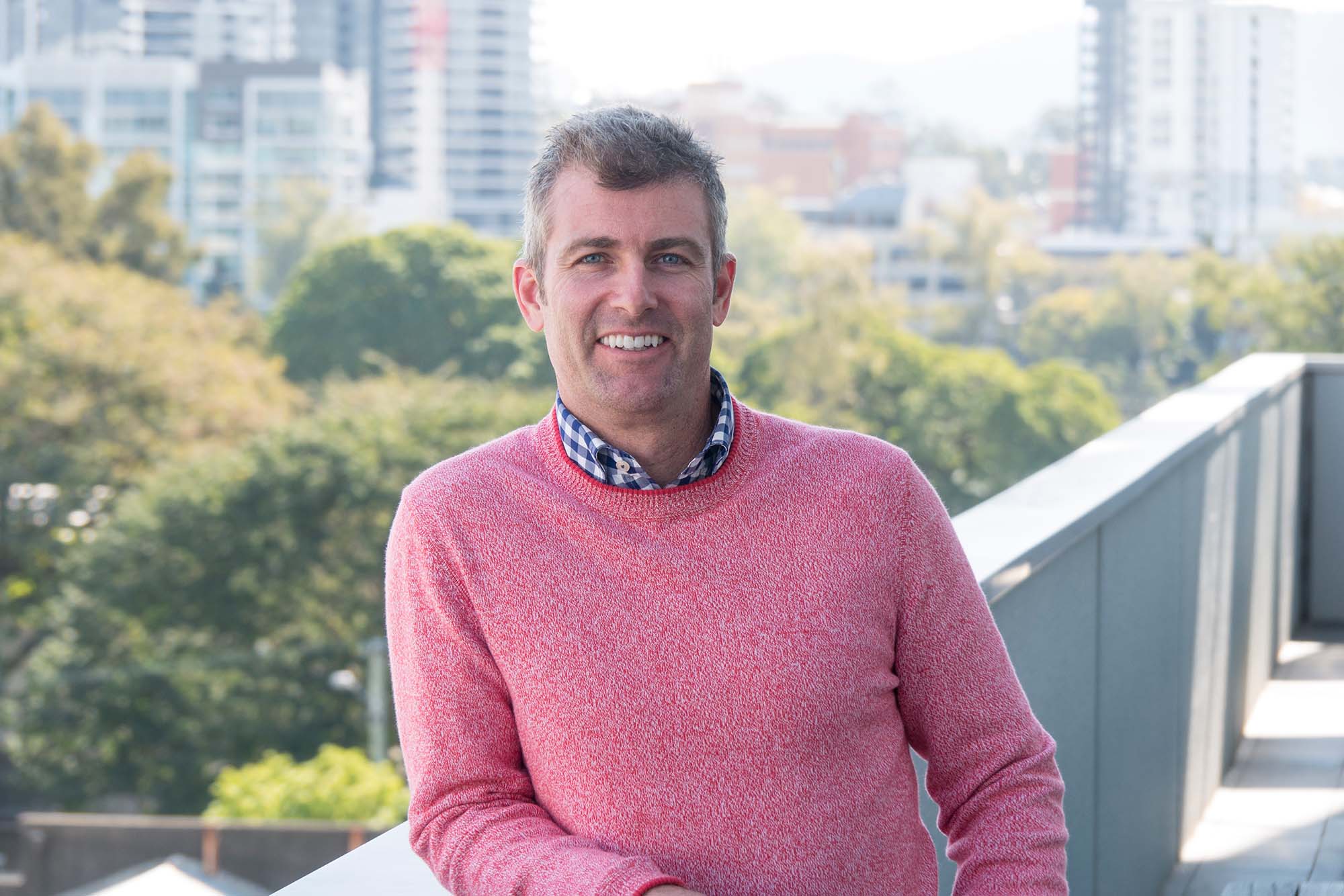 Jason Titman in pink sweater leaning with city scape in background