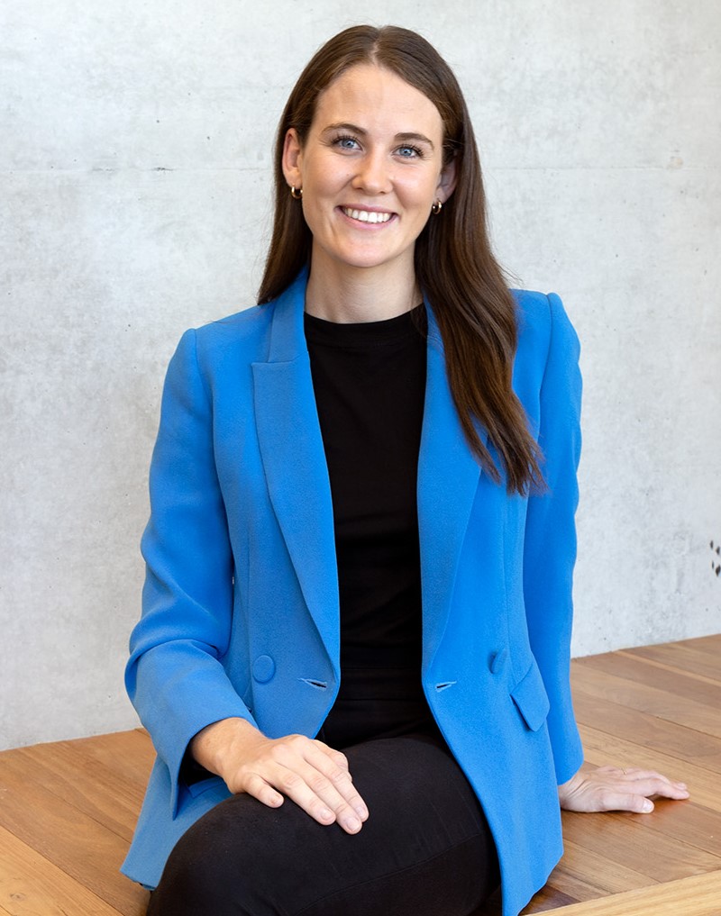 Hailey Brown founder of Vacayit wearing bright blue blazer sitting in front of concrete wall