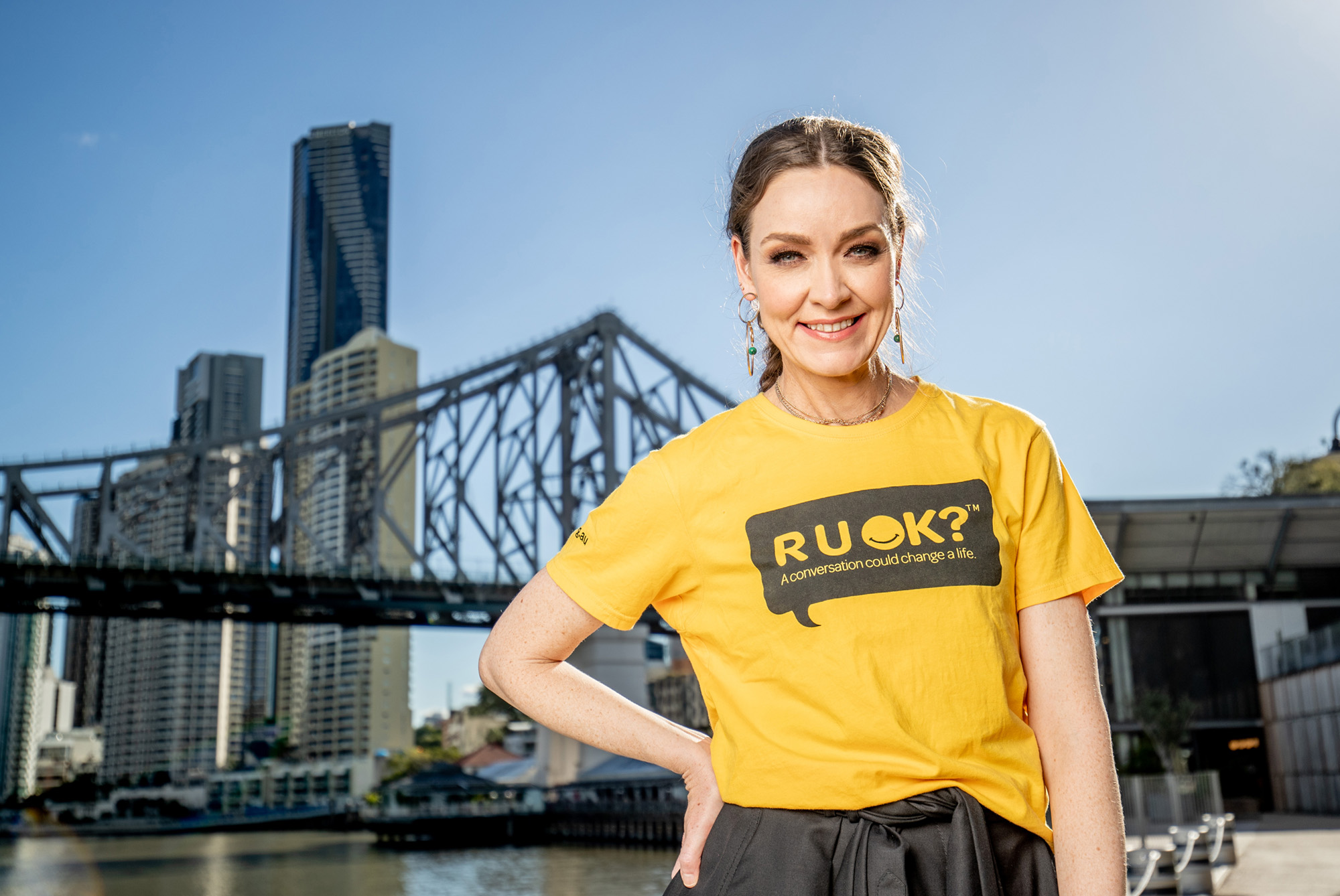 Aislinn Sharp wearing 'R U OK?' yellow tshirt in front of Brisbane skyline