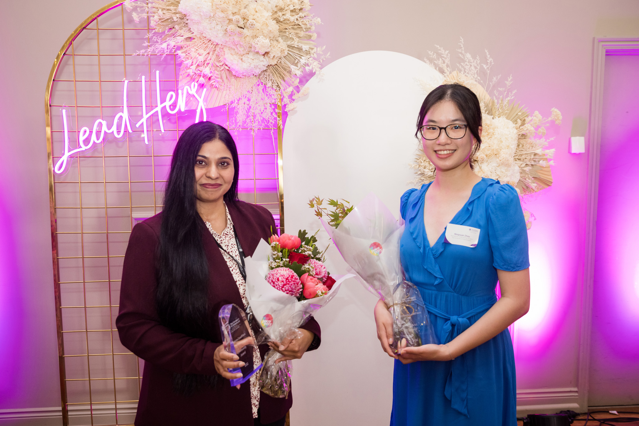 Award recipients Dr Sobia Zafar and Mingxuan Zhou standing in front of LeadHers neon sign