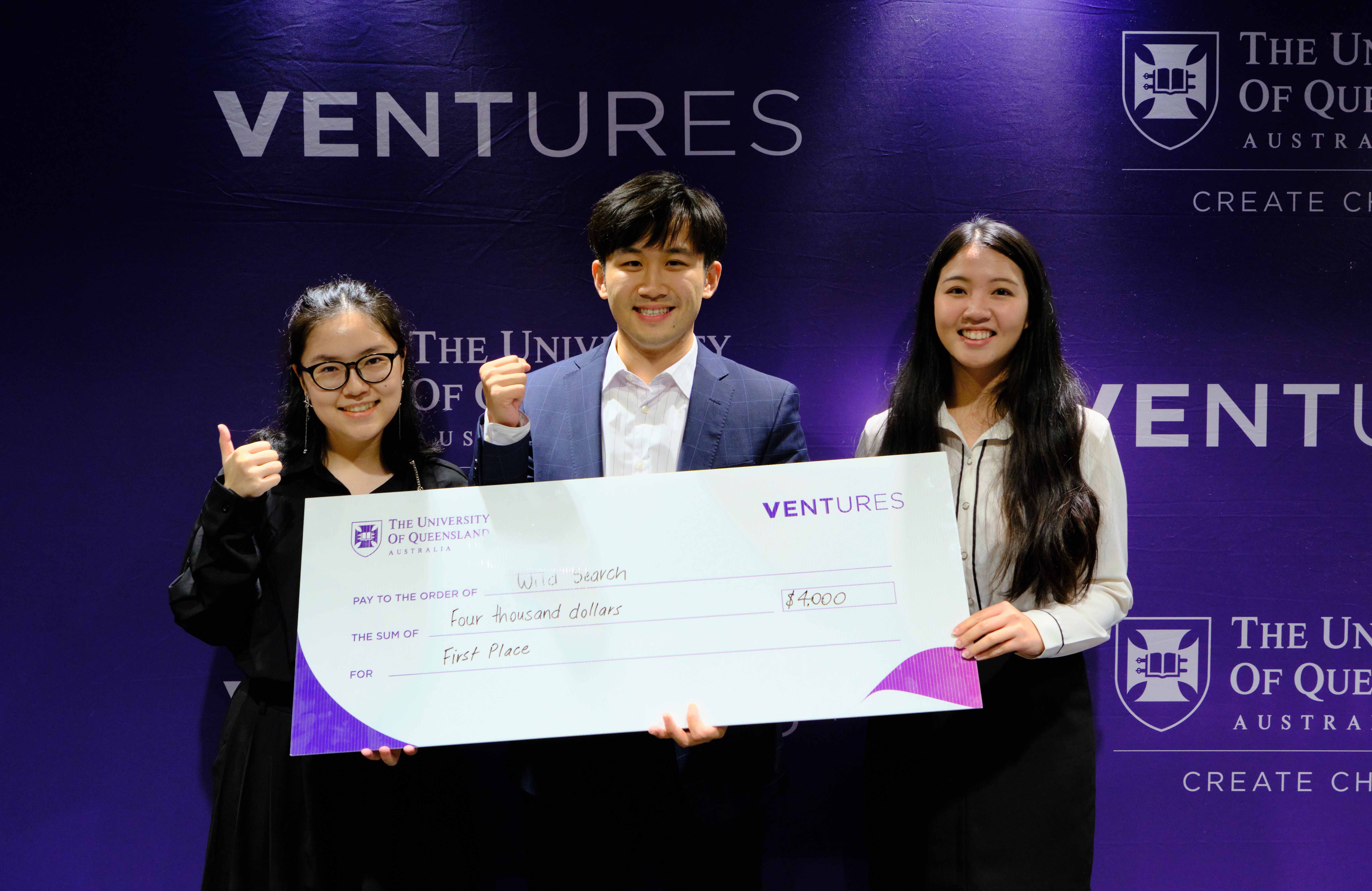 Winning team holding novelty cheque in front of purple media wall with UQ and Ventures logos