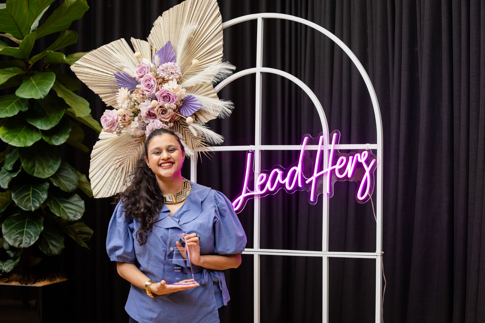 Hemanshi standing in front of a LeadHers neon sign