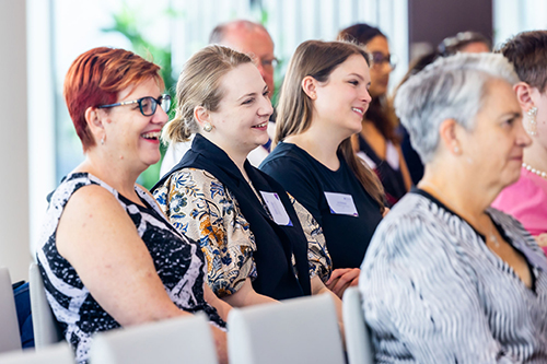 Photo of women of all different ages sitting in an audience and smiling