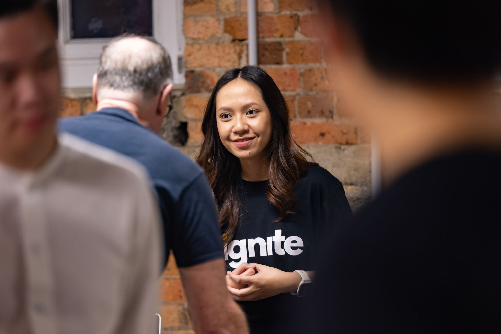 Image of a woman smiling as she talks to a person at an event. Can only see the back of the head of the other person. 
