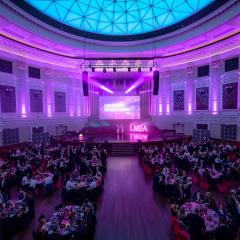 Brisbane City Council hall lit up in purple with a crowd of people watching the stage for the ceremony