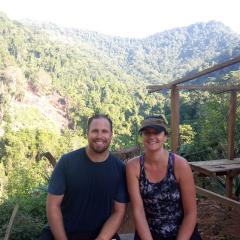 Merryn and Johnathon Strange sitting with a rural backdrop behind them: afternoon light, green mountains.