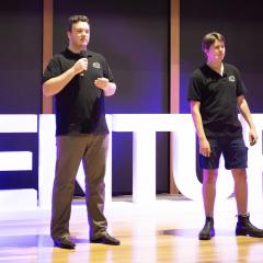 Oz Electric Vehicle team pitching on stage at the Ventures Industry Challenge in front of large Ventures staging letter 