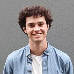 Thomas smiling and wearing white shirt under denim button down