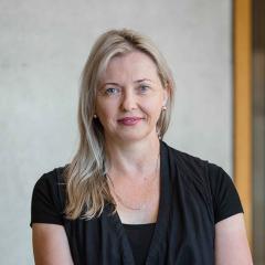Dr Jo'Anne Langham sitting crossed legged smiling without teeth at camera: blond long hair, black top. 