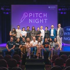 2022 Pitch Night founders sitting on stage in two tiers: on stairs and stairs with ilab Pitch Night sign in neon on the right. 