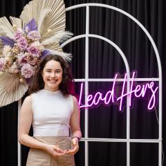 Clare Mahon standing in front of a LeadHers neon sign