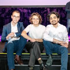 Herik Labs team sitting on steps to Pitch Night stage holding trophies 