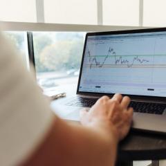 Person typing on laptop with financial graphs on screen