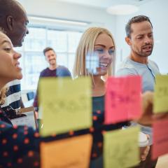 team of people standing in group brainstorming with colourful windownotes on a glass window
