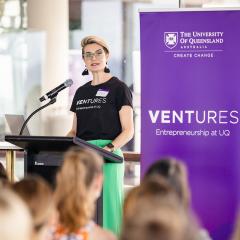women speaking at podium with audience in foreground and purple UQ Ventures banner behind