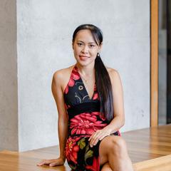 Dr Tran sitting on a wooden seat with a concrete wall behind her in a modern neck halter dress. 