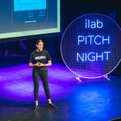 Hailey Brown pitching on stage with neon light behind her at the 2022 ilab accelerator pitch night