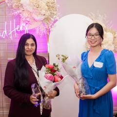 Award recipients Dr Sobia Zafar and Mingxuan Zhou standing in front of LeadHers neon sign