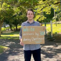 Marcus holding up cardboard sign reading 'wate increases by 30% during Christmas'