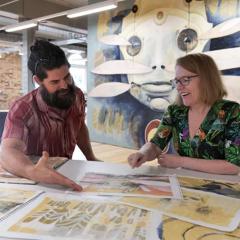 Street artist and UQ AI researcher collaborating at table 