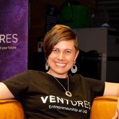 Sam Jockel sitting on an orange couch with the purple Ventures sign behind her